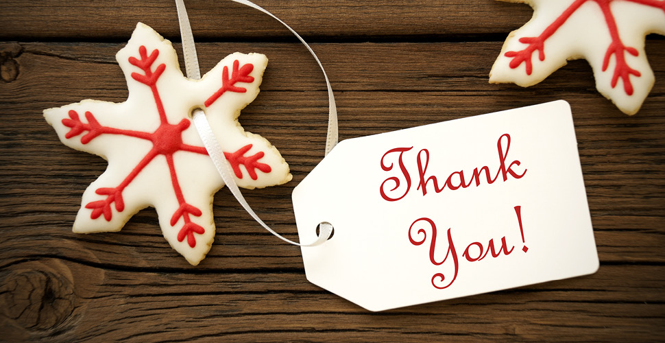 a sugar cookie decorated in white and red frosting in the shape of a snow flake. a thank you tag is attached to the snowflake cookie